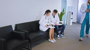 Kameranın önünde genç hemşire adam ve meslektaşı kadın doktor hastane koridorunda yürüyorlar ve hasta geçmişinin bir kısmını tartışıyorlar diğer hastane doktoru ve hemşireler