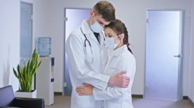 Parlak hastane koridorunda güvenlik maskesi takmış iki doktor birbirlerine sarılıyorlar. Üzgün bir yüzleri var.