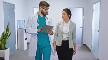 Hastanedeki güzel kadın hasta, hastane koridorunda yürüdükleri sağlık kontrolünden sonra doktorla sohbet ediyor ve dijital tablete bakıyor. ARRI 'de çekilen