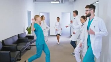 Karizmatik doktorlar ve hemşireler hastane koridorunda heyecanlı bir şekilde dans ediyorlar.