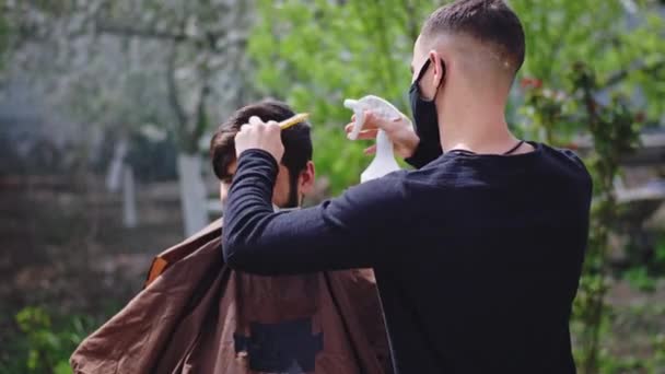 在家中的隔离病房里，一个英俊的男人在花园里剪头发，他的朋友开始用水喷洒科迪夫2019的头发概念. — 图库视频影像