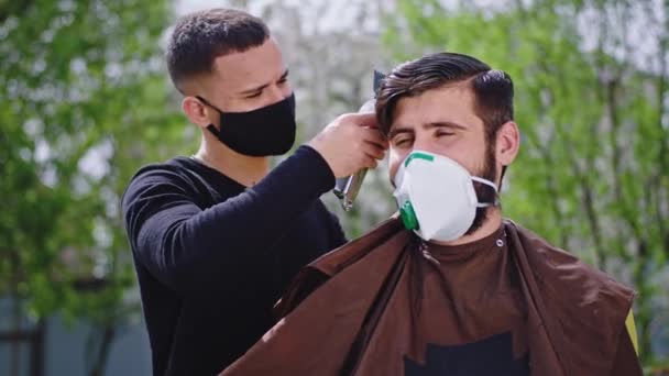 庭の外の家で保護マスクを持つ男は髪をカットするためにヘアクリッパーを使用して隔離された専門の理髪店の男でヘアカットを持っています — ストック動画