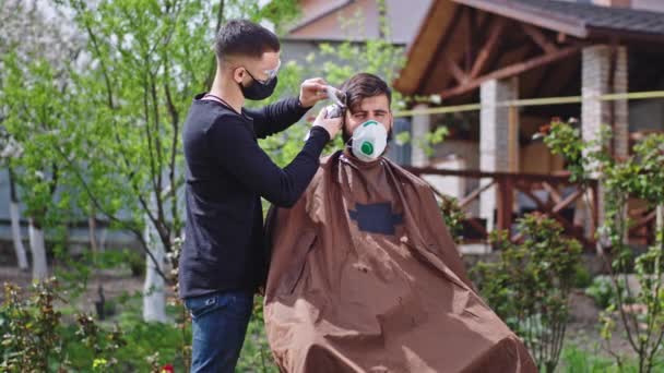 Zonnige dag in de tuin kapper man maak een kapsel in de tuin voor een man die ze dragen beschermende Coronavirus 2019 — Stockvideo