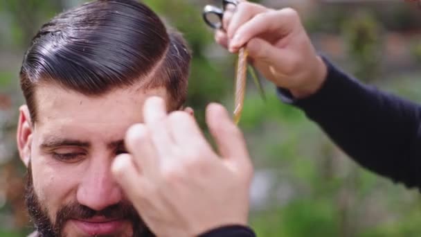 Carismático hombre primer plano de la cámara tienen un tiempo de corte de pelo en el jardín exterior en casa peluquero utilizando las tijeras para cortar el pelo profesional — Vídeos de Stock