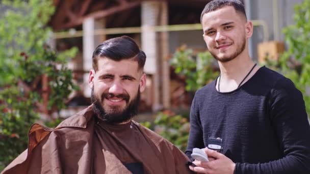 Lá fora, em casa, no jardim, caras bonitos olhando diretamente para a câmera e sorrindo grande, eles fazem o corte de cabelo enquanto ficam em casa — Vídeo de Stock