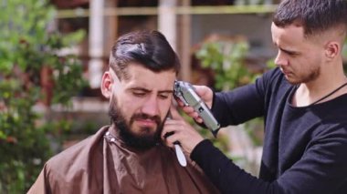 Güneşli bir günde, bir berber, saçlarını kesmek için elektronik makas kullanıyor.