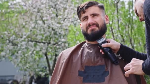 In the garden at home guy doing the beard barber man take the electronic clipper and cut carefully the beard — Stock Video