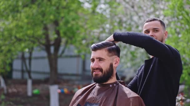 Lachende grote man hebben een kapsel tijd thuis in de tuin professionele kapper man met behulp van een schaar om het haar te knippen — Stockvideo