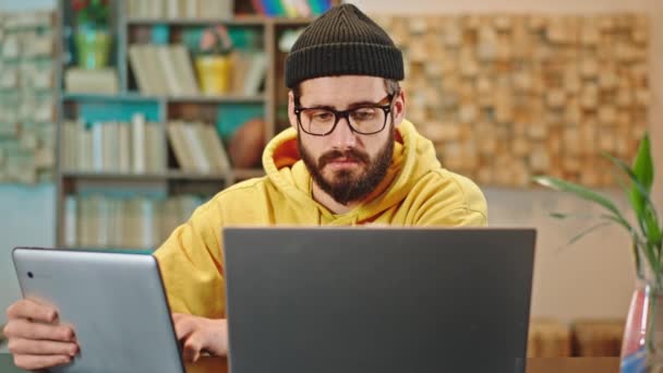 Ung kille med en smart glasögon som arbetar online hemifrån han använder den elektroniska surfplattan och laptop samtidigt för att avsluta sitt arbete — Stockvideo