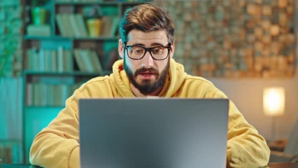 Ev ofisinden konsantre bir adam tüm ofislerle çevrimiçi bir toplantı yapıyor. Kameranın önünde dizüstü bilgisayardan bir şey anlatıyor. 4k — Stok video