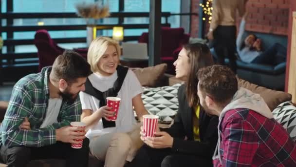 Szünet egy modern irodai stúdióban a szünetben a fiatalok szocializáló kávézás közben ül a kanapén — Stock videók