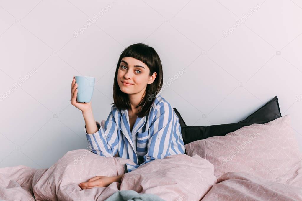 Hipster girl lounging in bed with coffee