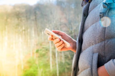 Sonbahar ağaç arka planda bir smartphone kullanırken parkta yürüyen bir esmer kadın bir düşük açılı fotoğraf. Yumuşak odak, rüya gibi bak. Teknoloji ve modern yaşam kavramı.