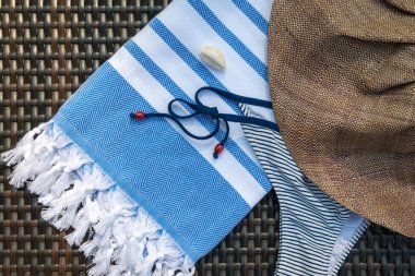 Beyaz ve mavi Türk peştemal düz yatıyordu yaz aksesuarları close-up kavramı / havlu, bikini, beyaz deniz kabuklarını ve hasır şapka bir rattan tembel.