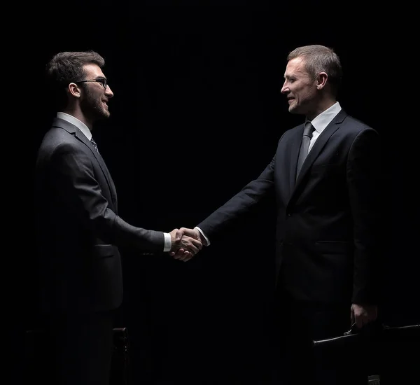 Two cheerful businessman shaking hands and looking at each other