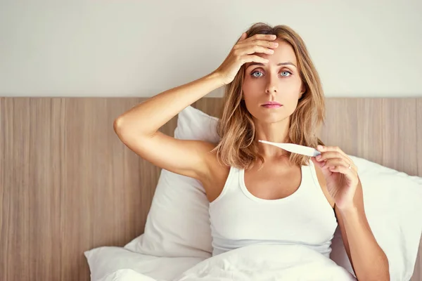 Kvinna på sängen håller termometer — Stockfoto