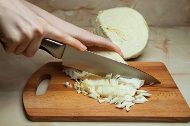 Mutfaktaki tahta tahtada lahana yapraklarını kesen bıçaklı bir kadın eli. Sağlıklı beslenme ve yaşam tarzı.