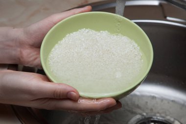 Kız, tembel lahana rulolarını hazırlamak için soğuk musluk suyunun altında pirinç yıkıyor.