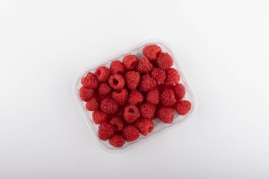 Beyaz arka planda izole edilmiş plastik kutuda taze ahududu..