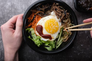  Kore yemeği bibimbap 'ı. Üst görünüm kapalı. Kore çubuklarını tutan eller.