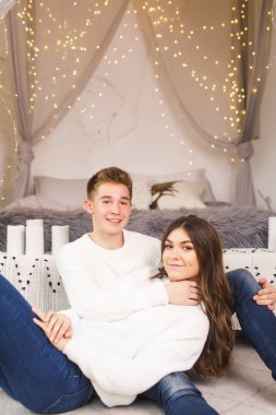 Güzel beyaz bir odada, yatakta oturmuş gülümseyen genç bir çift.