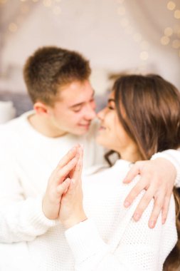 Güzel beyaz bir odada, yatakta oturmuş gülümseyen genç bir çift.