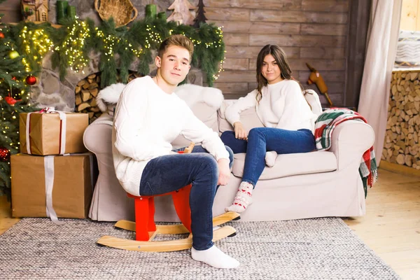 クリスマスツリーを背景にベッドの上の美しい部屋に座って笑っている若い美しいカップル — ストック写真