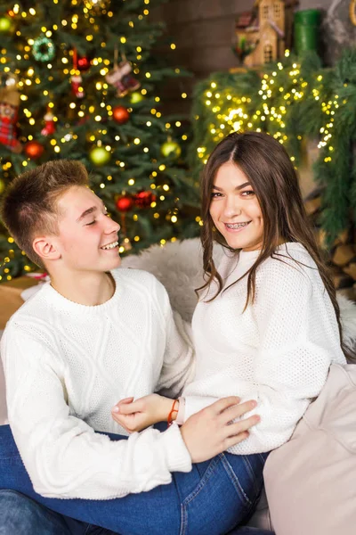 一对年轻漂亮的夫妇坐在床上的一间漂亮的房间里 靠着圣诞树 微笑着 — 图库照片