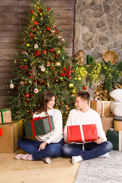 Young beautiful couple sits on a background of the Christmas tree in their hands holding gifts and smiling