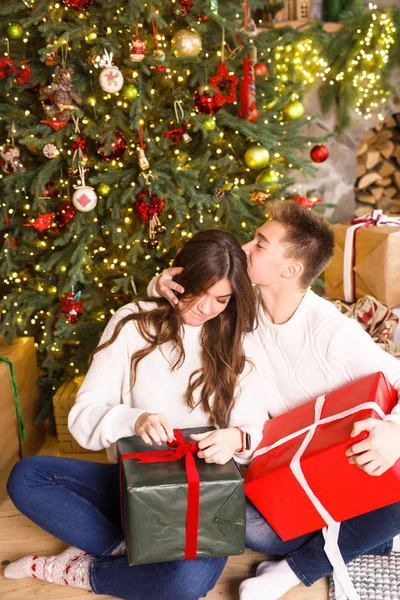 Young beautiful couple sits on a background of the Christmas tree in their hands holding gifts and smiling