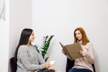 Genç ve güzel kadınlar ellerinde kahve fincanlarıyla güzellik salonunda oturuyorlar.