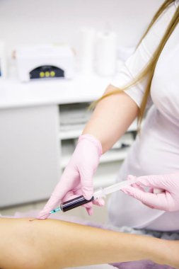 Beyaz önlüklü hemşire ve pembe eldivenli hemşire hastanın eline vitamin ve kan enjekte ediyor.