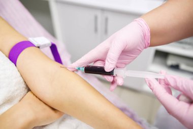 Beyaz önlüklü hemşire ve pembe eldivenli hemşire hastanın eline vitamin ve kan enjekte ediyor.