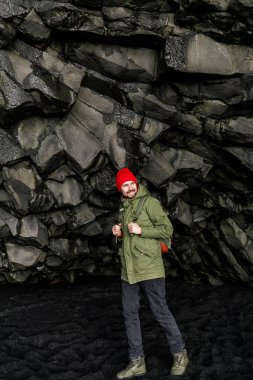 yakışıklı turist dağdaki mağarada siyah kumda yürüyor.