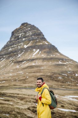 İzlanda dağlarının önündeki çimlerde yürüyen yakışıklı genç adam.