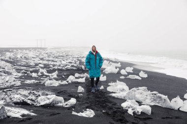 beautiful young man walking on winter black sand beach background