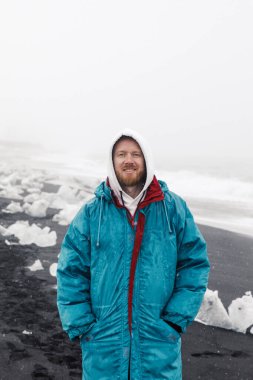 beautiful young man walking on winter black sand beach background