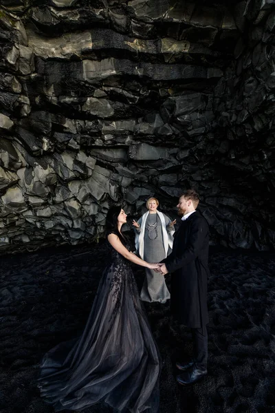 アイスランドの野外結婚式で結び目を結ぶ美しい若い女性と男黒の洞窟 — ストック写真