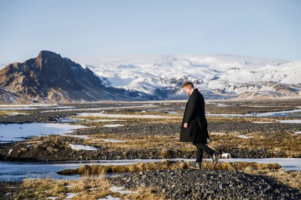 handsome man waking on black land on Iceland on mountains background