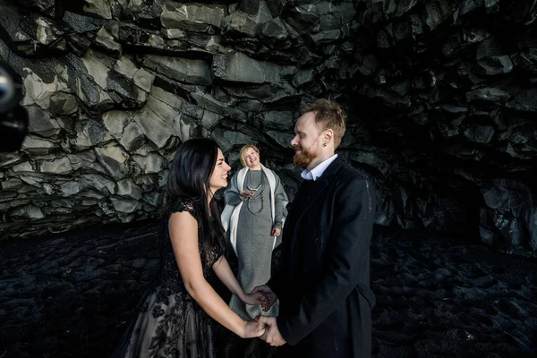 beautiful young woman and man tying the knot in an open air wedding ceremony in Iceland black cave