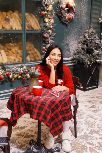 若い美しいブルネットの女の子赤いセーターと白いパンツパン屋の窓を背景にパリの路上でお茶を飲む — ストック写真