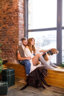 Genç ve güzel bir çift pencerede iki köpekle oturuyor.