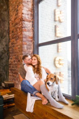 Genç ve güzel bir çift pencerede iki köpekle oturuyor.