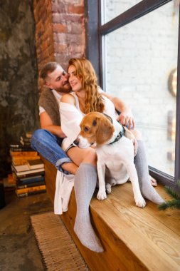 Genç ve güzel bir çift pencerede iki köpekle oturuyor.