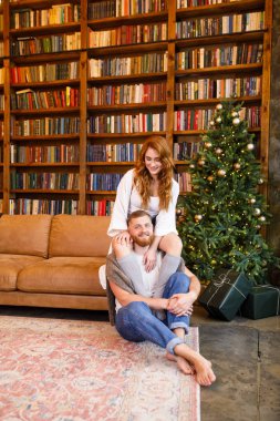 Genç ve güzel bir çift kütüphanenin arka planında, yatakta oturuyor ve dairenin tavan arası tarzında kitapları var.