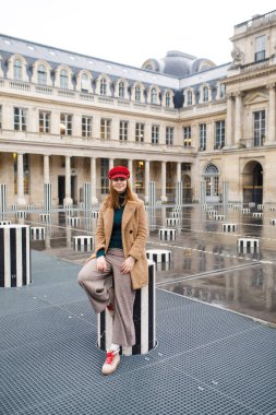 Paris 'te bir meydanda kahverengi paltolu ve kırmızı şapkalı güzel bir kız duruyor.