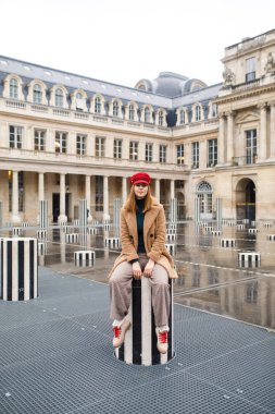 Paris 'te bir meydanda kahverengi paltolu ve kırmızı şapkalı güzel bir kız duruyor.