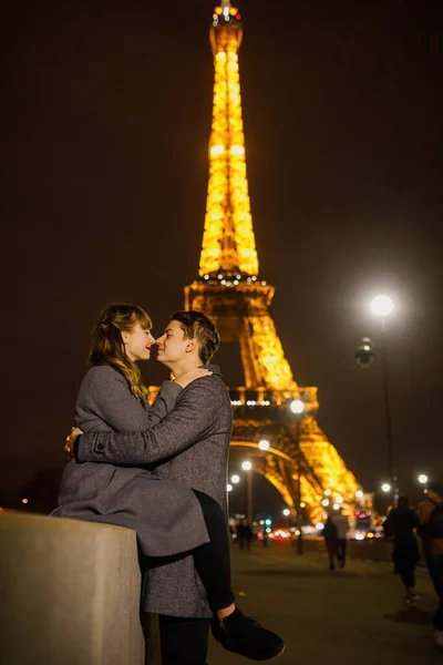 一对年轻漂亮的夫妇穿着时髦的衣服 一个穿着灰色外套的女孩 一个穿着灰色外套的男人 深夜在巴黎的埃菲尔铁塔附近散步 — 图库照片