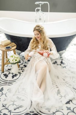 Genç, sarışın bir gelinin portresi. Banyoda bir şişe şampanyayla.