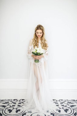Beyaz bir odada buketi olan güzel sarışın bir gelinin portresi.